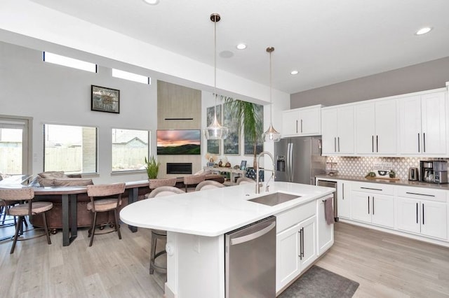 kitchen with decorative backsplash, light wood-style flooring, appliances with stainless steel finishes, open floor plan, and a sink