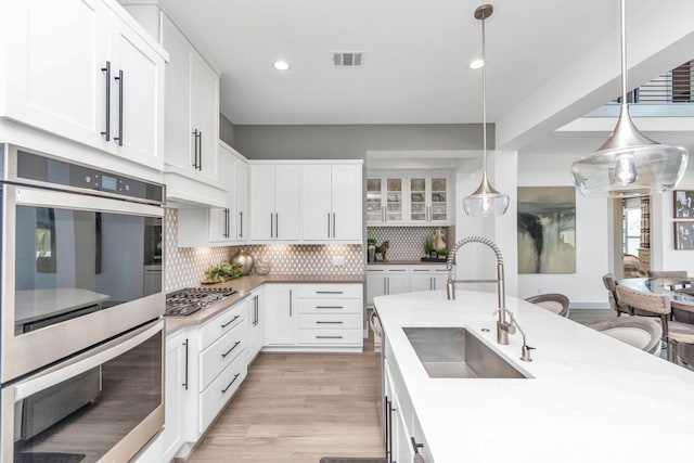 kitchen featuring a sink, stainless steel appliances, light wood-style floors, white cabinetry, and backsplash