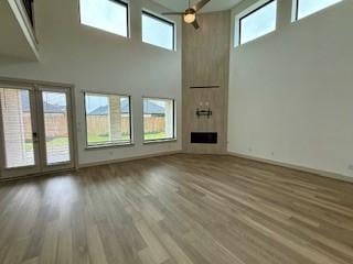 unfurnished living room featuring a large fireplace, a high ceiling, wood finished floors, and baseboards