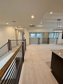 hall with recessed lighting, light colored carpet, and an upstairs landing