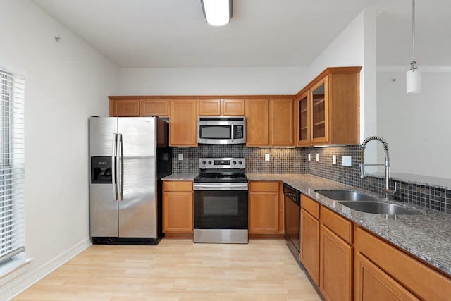 kitchen featuring dark stone counters, appliances with stainless steel finishes, brown cabinetry, and a sink