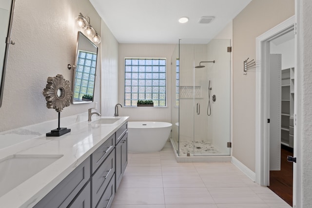 bathroom with a stall shower, a sink, double vanity, a soaking tub, and a spacious closet