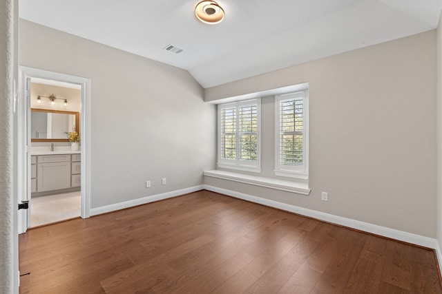 empty room with visible vents, wood finished floors, baseboards, and vaulted ceiling