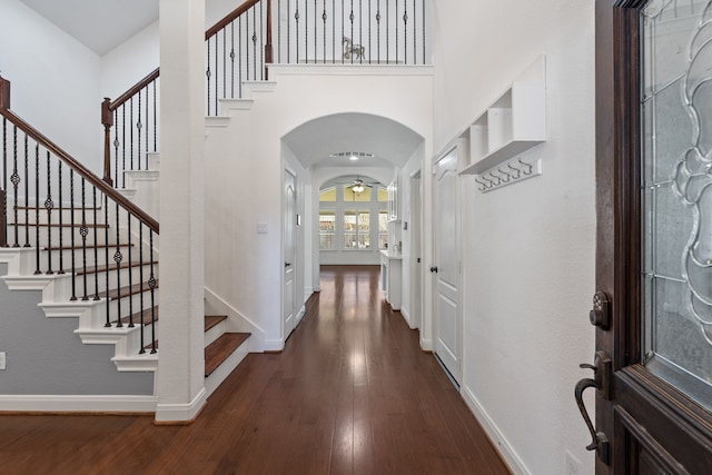 foyer featuring dark wood-style floors, baseboards, arched walkways, ceiling fan, and a towering ceiling