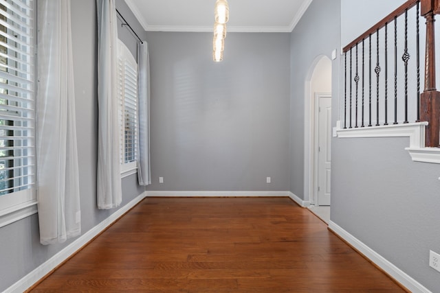 spare room with crown molding, wood finished floors, arched walkways, and baseboards