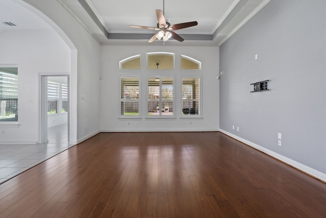 empty room with arched walkways, crown molding, a tray ceiling, and hardwood / wood-style floors