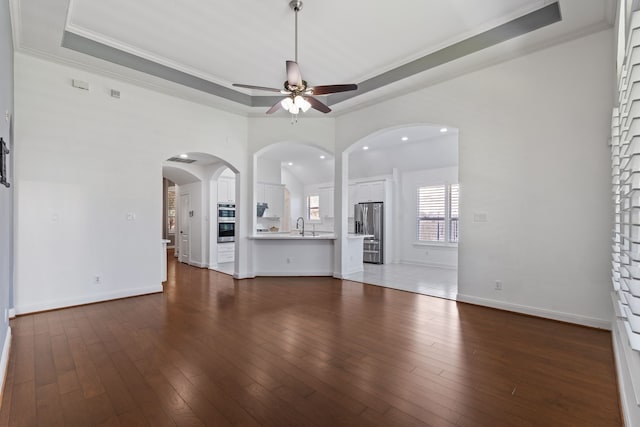 unfurnished living room with dark wood-style floors, baseboards, a raised ceiling, and ceiling fan