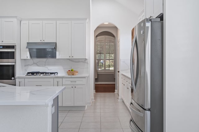 kitchen featuring light stone counters, stainless steel appliances, light tile patterned flooring, white cabinets, and decorative backsplash