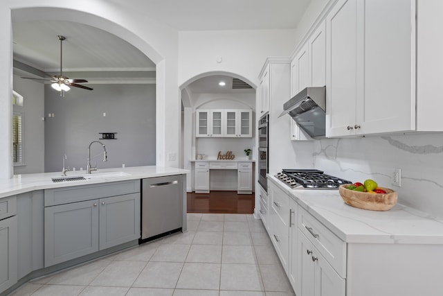 kitchen featuring a ceiling fan, a sink, light stone counters, appliances with stainless steel finishes, and wall chimney exhaust hood