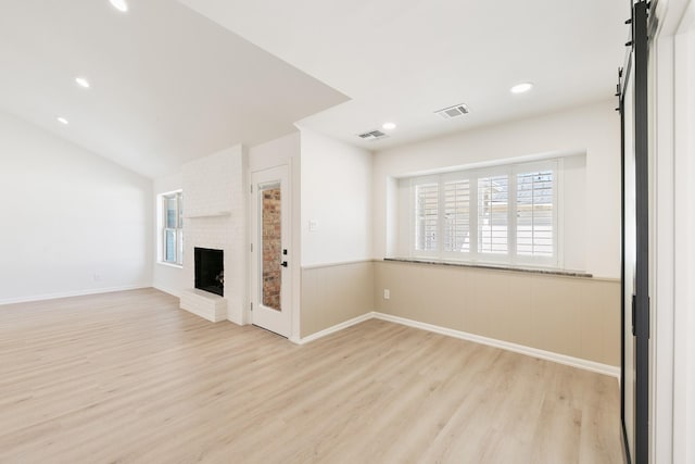 unfurnished living room with visible vents, a brick fireplace, wood finished floors, and a wainscoted wall