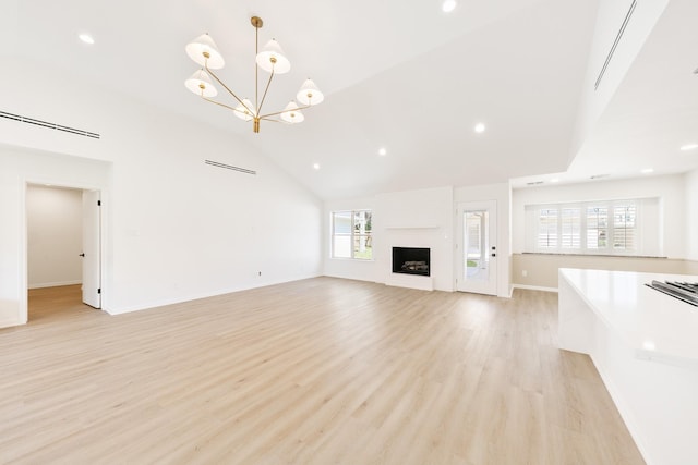 unfurnished living room with high vaulted ceiling, an inviting chandelier, a fireplace, light wood finished floors, and baseboards