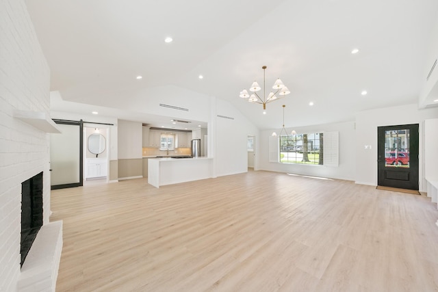 unfurnished living room featuring a barn door, a brick fireplace, a notable chandelier, and light wood-style floors