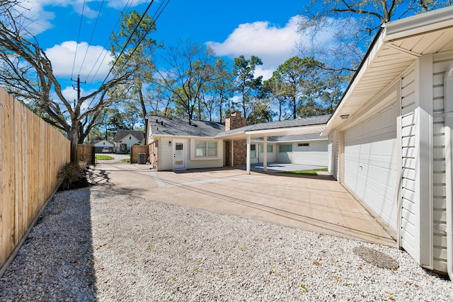 rear view of property featuring gravel driveway, a patio, fence, and a chimney