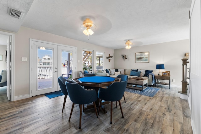 dining space featuring baseboards, visible vents, wood finished floors, a textured ceiling, and french doors