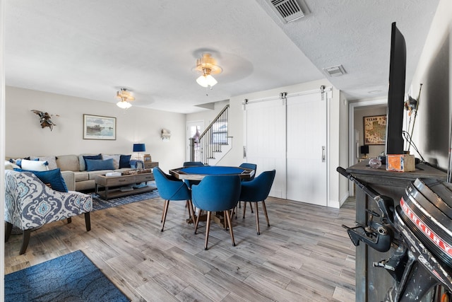 dining room with a textured ceiling, a barn door, light wood-type flooring, and visible vents