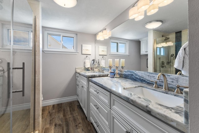 full bathroom with wood finished floors, a sink, baseboards, a shower stall, and double vanity