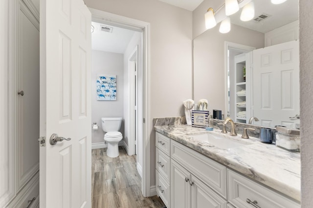 bathroom with toilet, wood finished floors, vanity, and visible vents