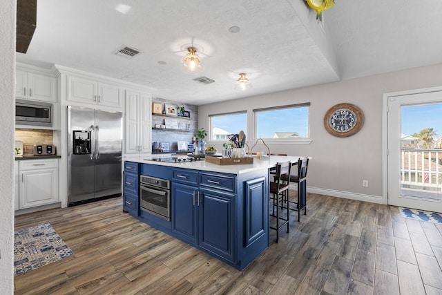 kitchen with a breakfast bar area, wood finished floors, white cabinetry, appliances with stainless steel finishes, and blue cabinetry