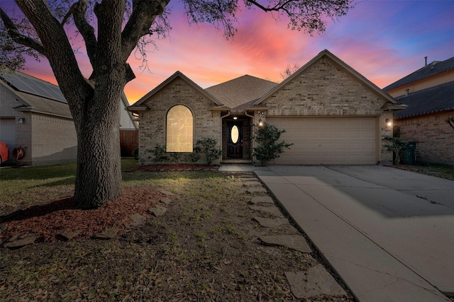 french country home featuring driveway, brick siding, roof with shingles, and an attached garage