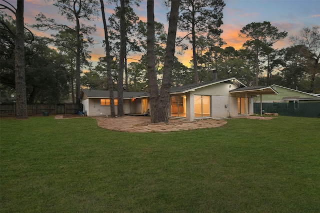 back of house at dusk featuring a yard and fence