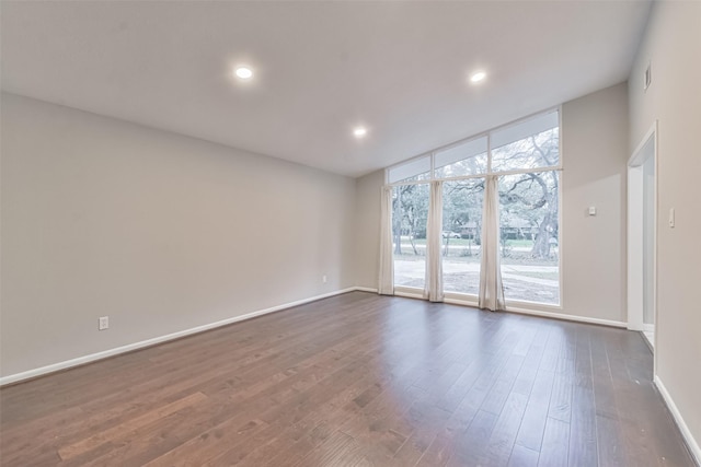 spare room featuring dark wood-style flooring, a wall of windows, recessed lighting, and baseboards