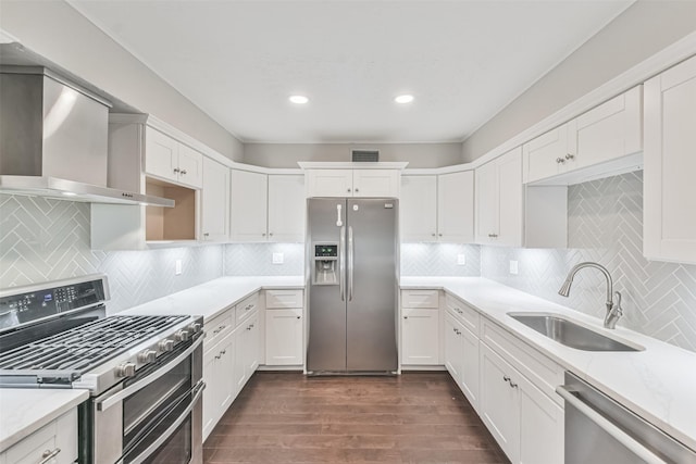 kitchen featuring white cabinets, appliances with stainless steel finishes, dark wood-type flooring, wall chimney range hood, and a sink