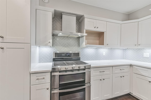 kitchen with range with two ovens, white cabinets, wall chimney range hood, and tasteful backsplash