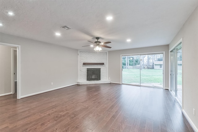 unfurnished living room with dark wood-style floors, a brick fireplace, a textured ceiling, and a ceiling fan