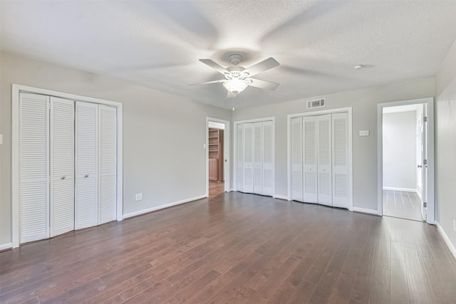 unfurnished bedroom with a textured ceiling, dark wood-type flooring, visible vents, baseboards, and multiple closets