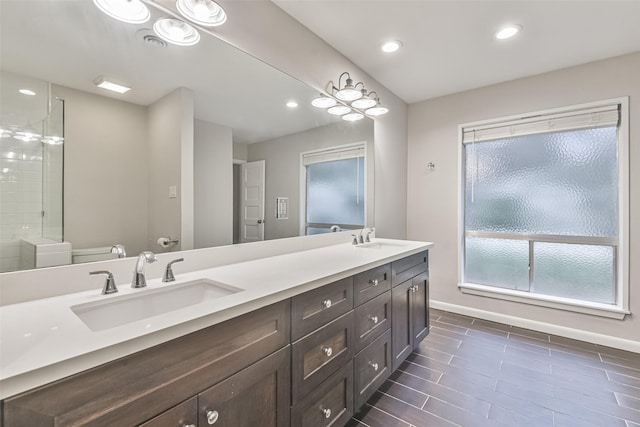 full bath featuring double vanity, a sink, toilet, and baseboards