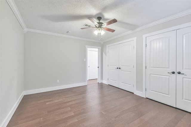 unfurnished bedroom featuring crown molding, a textured ceiling, two closets, and wood finished floors