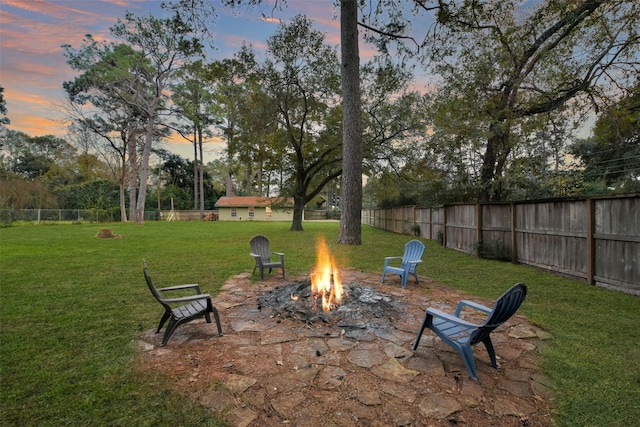 patio terrace at dusk with fence, a fire pit, and a yard