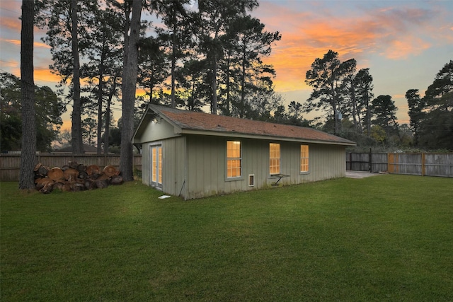 back of property at dusk with an outbuilding, a yard, and fence