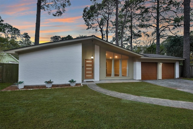 view of front facade with aphalt driveway, a yard, stucco siding, an attached garage, and fence