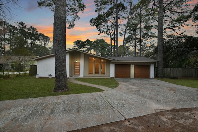 mid-century modern home with driveway, a garage, fence, and a front lawn