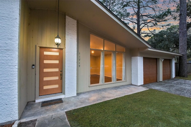 exterior entry at dusk with a garage and brick siding