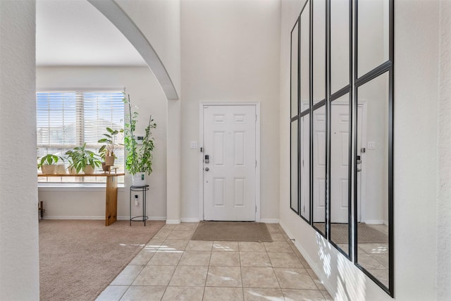 carpeted entryway with arched walkways, a high ceiling, baseboards, and tile patterned floors