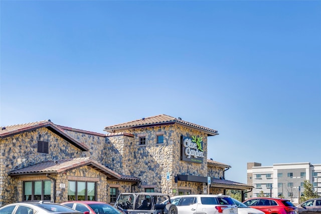 view of front of property featuring stone siding, uncovered parking, and a tiled roof