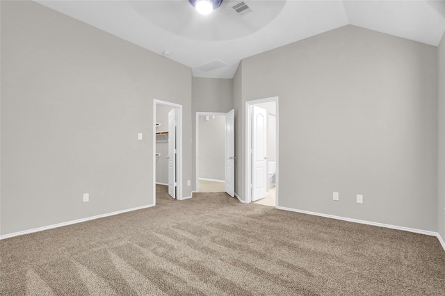 unfurnished bedroom featuring baseboards, visible vents, vaulted ceiling, a walk in closet, and carpet flooring