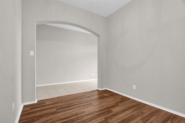 empty room with baseboards, arched walkways, and wood finished floors