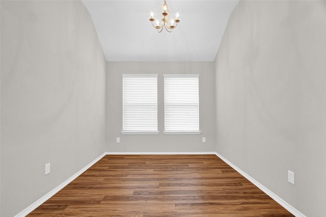 unfurnished room featuring a notable chandelier, baseboards, lofted ceiling, and wood finished floors