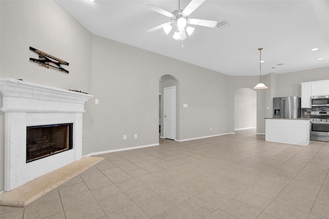 unfurnished living room featuring visible vents, a ceiling fan, a high end fireplace, arched walkways, and baseboards