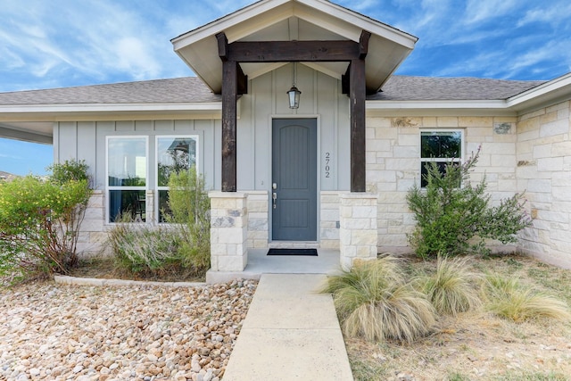 doorway to property featuring stone siding, board and batten siding, and roof with shingles