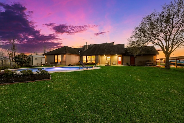 back of house at dusk featuring an outdoor pool, a lawn, an outbuilding, fence, and a patio area