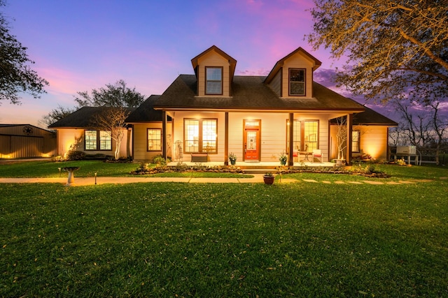 new england style home featuring covered porch and a lawn