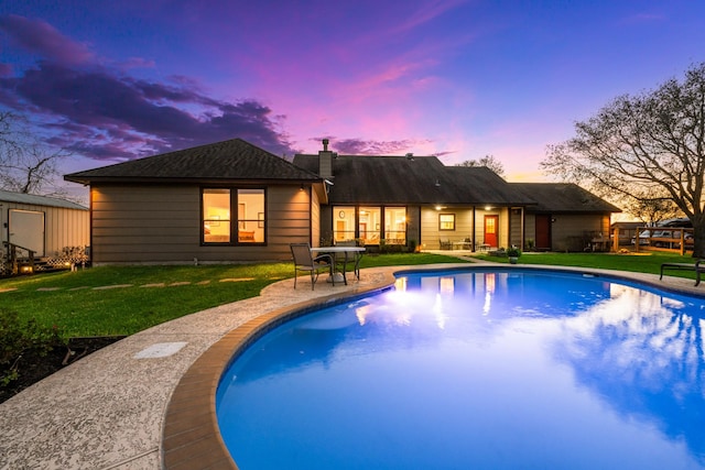 pool at dusk featuring an outbuilding, a yard, and an outdoor pool