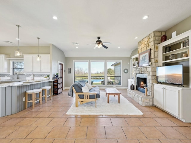 living area with light tile patterned floors, ceiling fan, a stone fireplace, recessed lighting, and baseboards