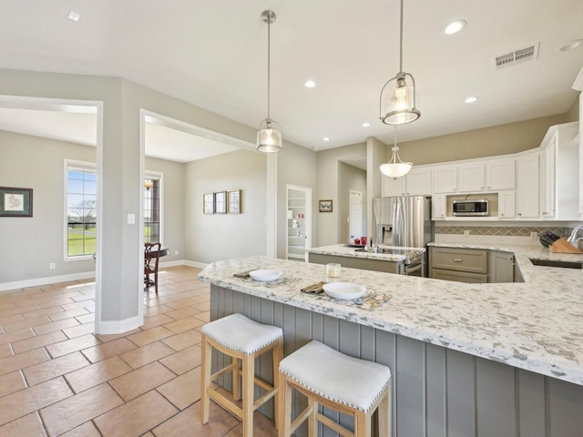 kitchen featuring light stone counters, stainless steel appliances, visible vents, backsplash, and a sink