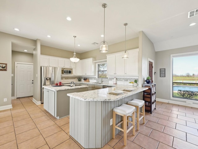 kitchen featuring visible vents, a kitchen island, appliances with stainless steel finishes, a peninsula, and a sink