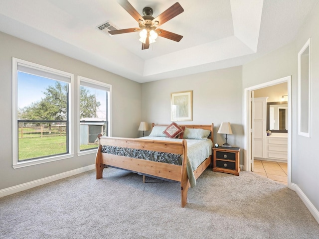 carpeted bedroom with ensuite bathroom, a tray ceiling, visible vents, and baseboards